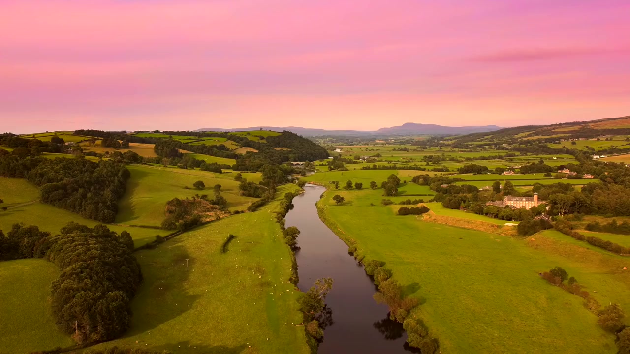 A river winding between green fields under a pink evening sky